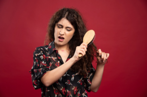 "A frustrated woman holding a tangled hairbrush, struggling to remove hair."